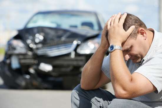 Upset driver beside a damaged car after an accident